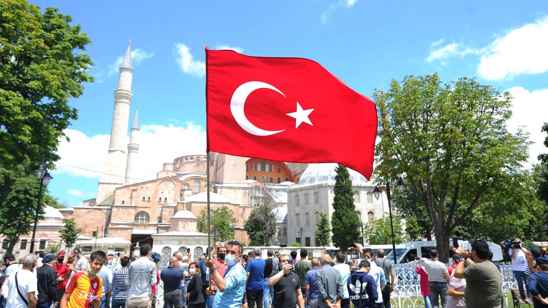 Blick auf die Hagia Sophia in Istanbul. Im Vordergrund weht eine türkische Flagge, die ein Mann auf dem Platz in die Höhe hält. Blick auf die Hagia Sophia in Istanbul. Im Vordergrund weht eine türkische Flagge, die ein Mann auf dem Platz in die Höhe hält.