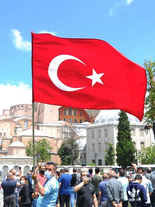 Blick auf die Hagia Sophia in Istanbul. Im Vordergrund weht eine türkische Flagge, die ein Mann auf dem Platz in die Höhe hält.
