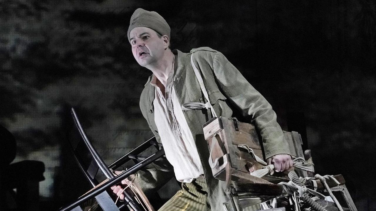 Mit vielen Gerätschaften beladen steht Wozzeck auf der Bühne Mit vielen Gerätschaften beladen steht Wozzeck auf der Bühne