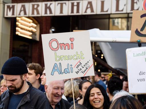 Eine Frau hält ein Schild hoch, auf dem steht: "Omi braucht Aldi".