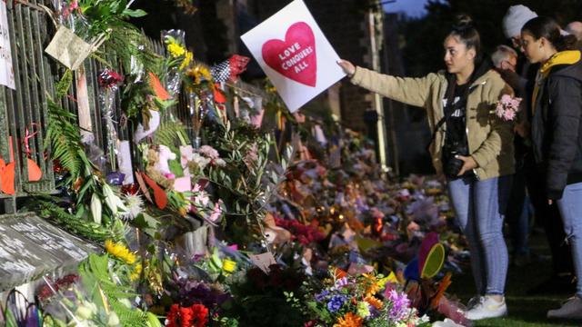 Eine Frau mit einem Herz-Transparent vor vielen Blumensträußen zum Gedenken an die Toten
