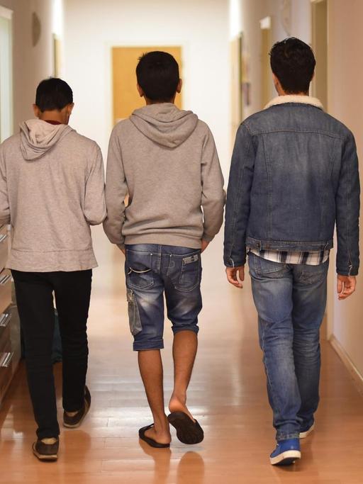 Drei Jugendliche gehen einen Flur entlang. Sie sind von hinten zu sehen.