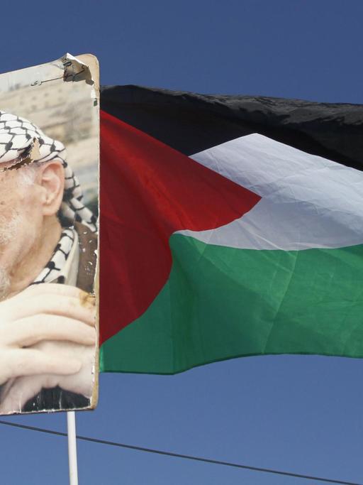 Ein Porträt von Palästinenserpräsident Arafat neben einer palästinensischen Flagge.
