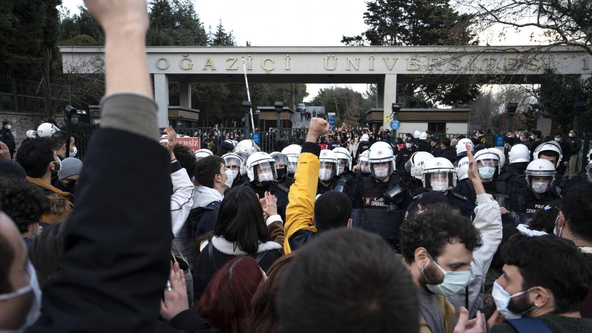 Protestierende stehen mit gereckten Fäusten vor behelmten Polizisten an der Boğaziçi-Universität Istanbul. Protestierende stehen mit gereckten Fäusten vor behelmten Polizisten an der Boğaziçi-Universität Istanbul.