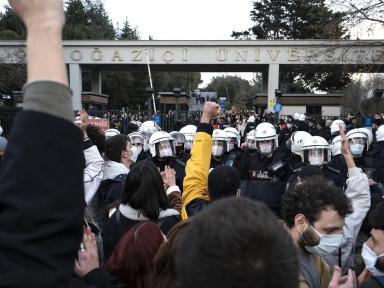 Protestierende stehen mit gereckten Fäusten vor behelmten Polizisten an der Boğaziçi-Universität Istanbul.