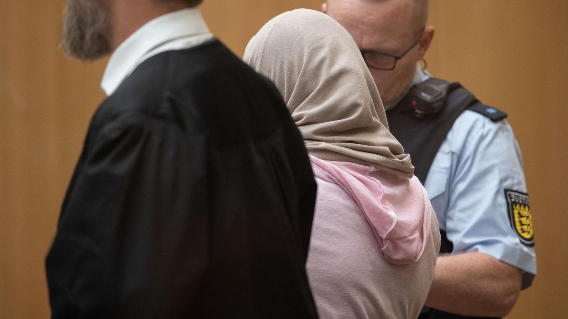Beim Prozess gegen eine mutmaßliche Islamistin vor dem Oberlandesgericht Stuttgart steht die Angeklagte im Gerichtssaal neben ihrem Anwalt und einem Justizmitarbeiter.