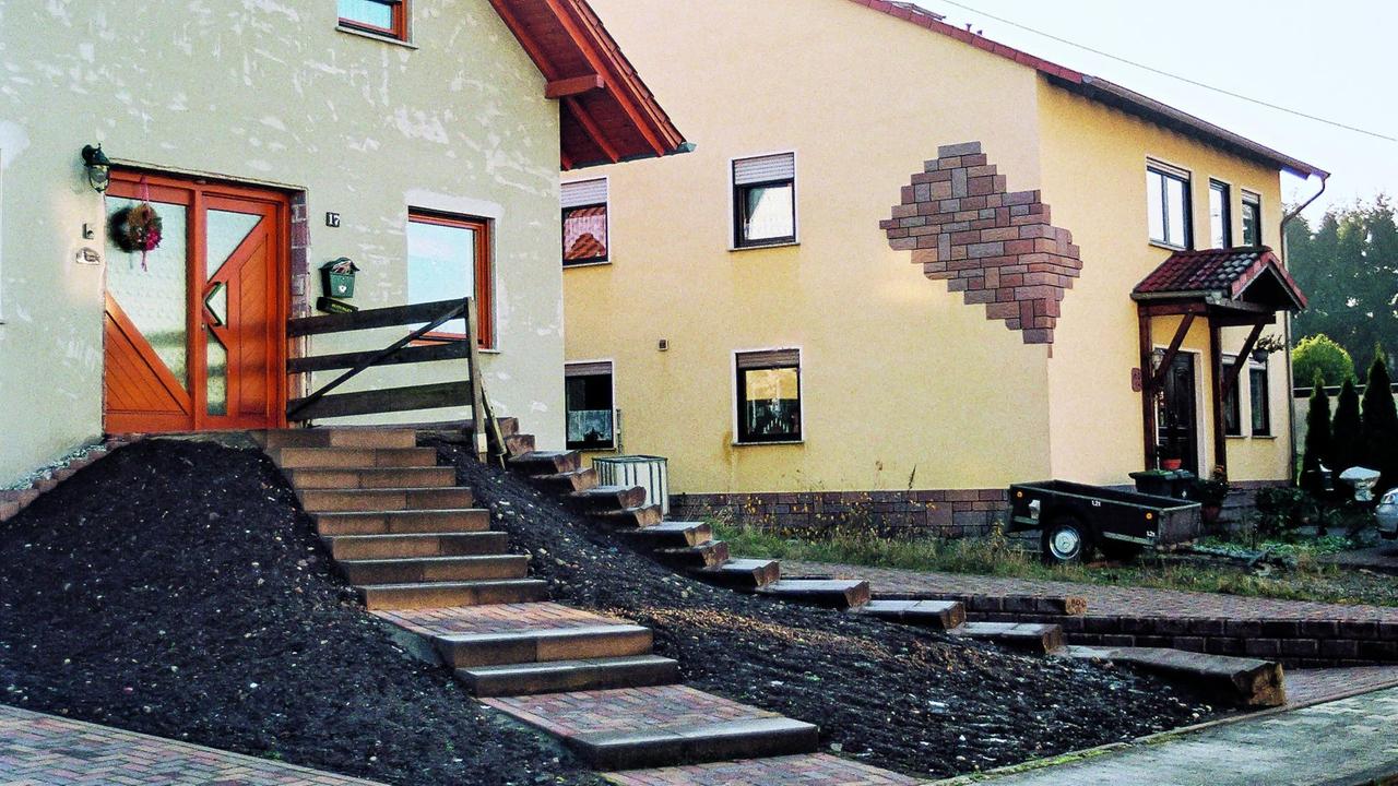 Einfamilienhaus mit einer Treppe auf einem aufgeschütteten Hügel, der zur Eingangstür führt.