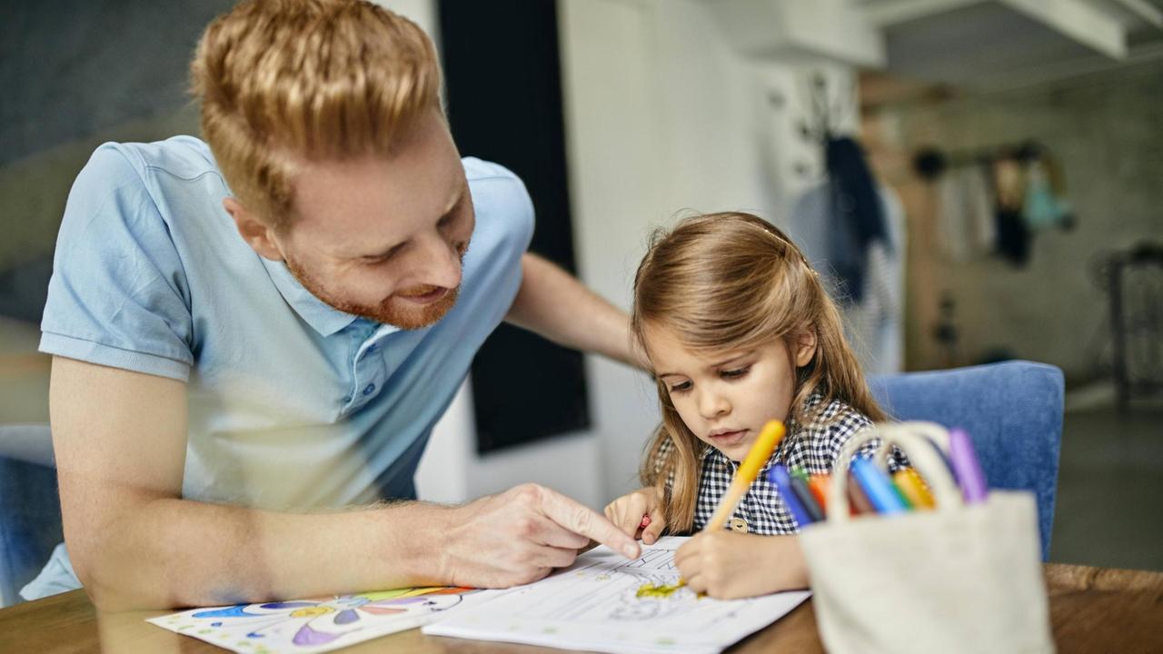 Ein Vater sitzt mit seiner Tochter an einem Tisch und malt Ein Vater sitzt mit seiner Tochter an einem Tisch und malt