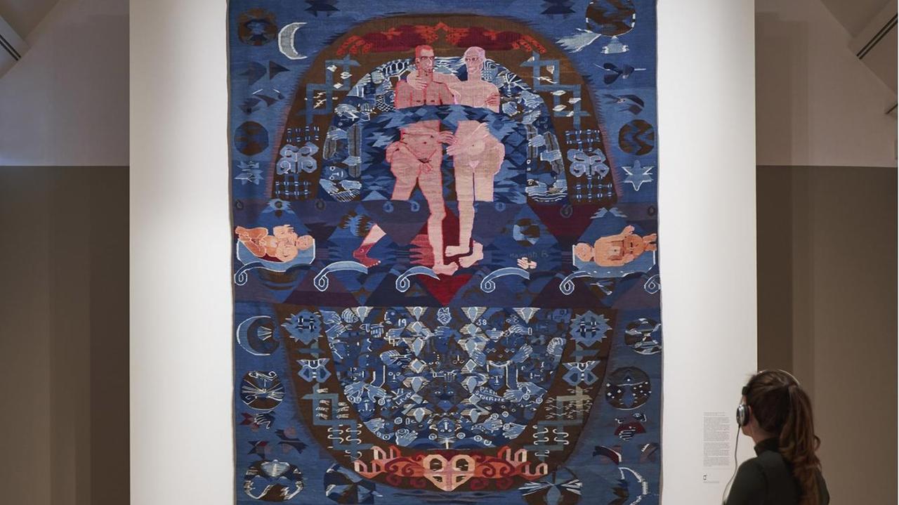 Auf dem Wandteppich an der Wand des Museums sieht man ein nacktes, sich umschlingendes Paar. Um dieses Paar herum ranken sich Köpfe, Hände, Werkzeuge. Rechts und links je ein Säugling. Es dominiert die Farbe blau, ein braunes Oval spannt sich wie ein großer Buchstabe O über die gesamte Fläche. Außerhalb erkennt man desweiteren Sterne und den Mond. Auf dem Wandteppich an der Wand des Museums sieht man ein nacktes, sich umschlingendes Paar. Um dieses Paar herum ranken sich Köpfe, Hände, Werkzeuge. Rechts und links je ein Säugling. Es dominiert die Farbe blau, ein braunes Oval spannt sich wie ein großer Buchstabe O über die gesamte Fläche. Außerhalb erkennt man desweiteren Sterne und den Mond.