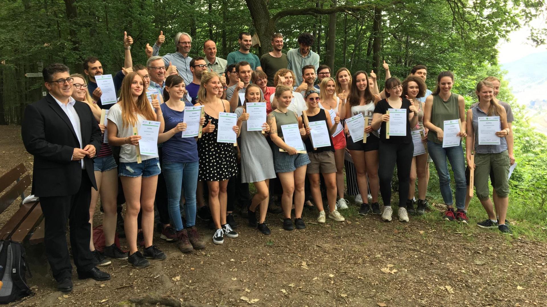 40 Umwelt- und Klimaschutz-Studenten stehen in einem Wald und halten ihre Urkunden in ihren Händen 40 Umwelt- und Klimaschutz-Studenten stehen in einem Wald und halten ihre Urkunden in ihren Händen
