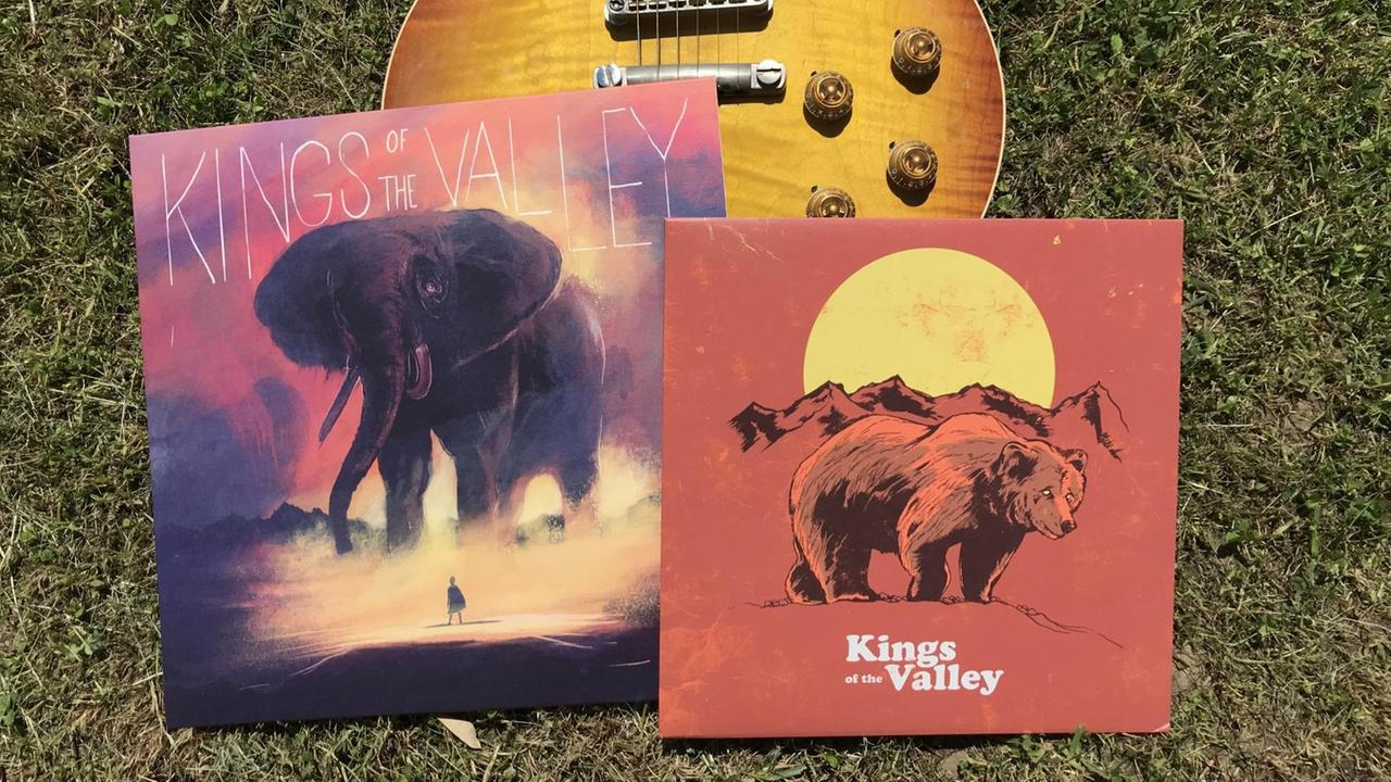 Zwei Vinyl-LPs mit bunten Covern liegen vor einer E-Gitarre auf dem Rasen. Zwei Vinyl-LPs mit bunten Covern liegen vor einer E-Gitarre auf dem Rasen.