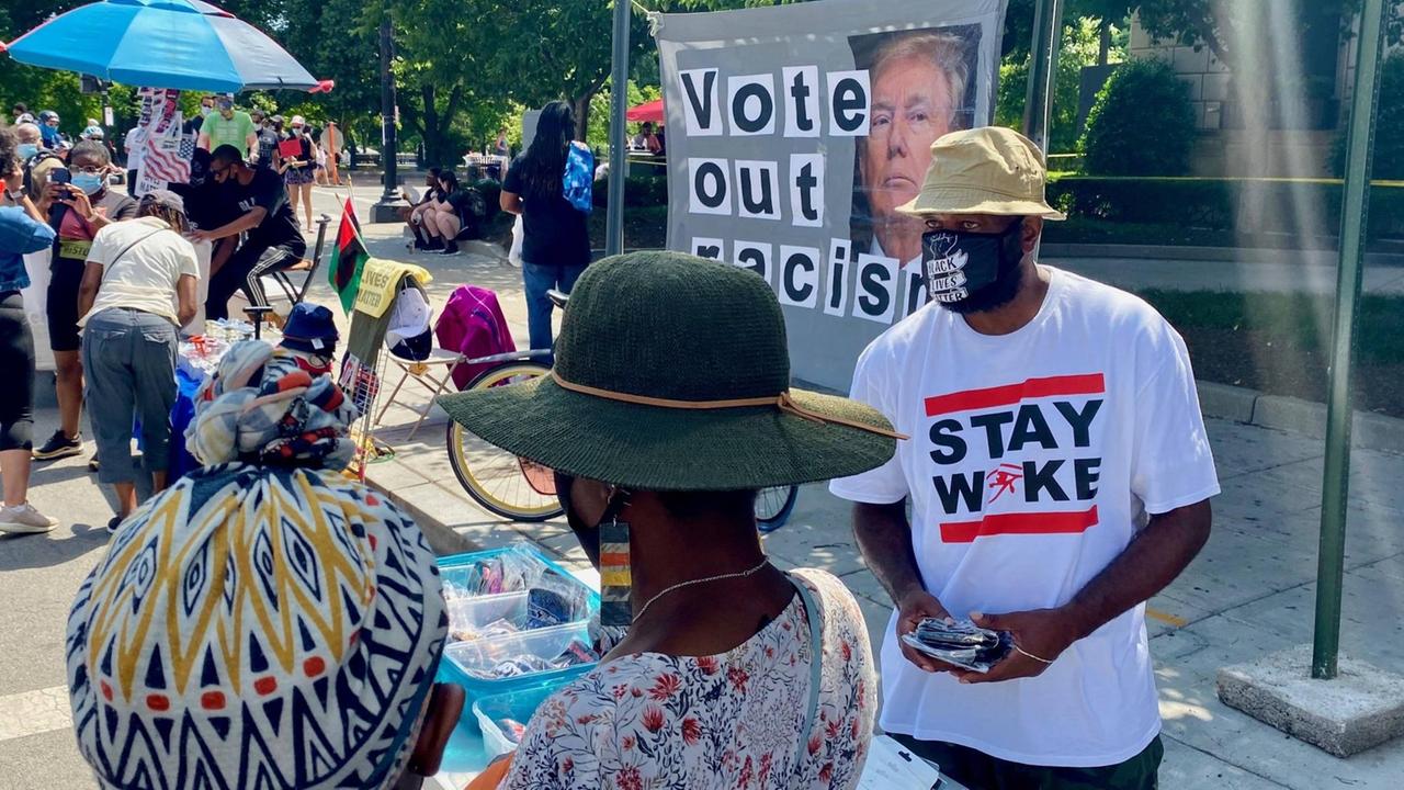 Ein Stand am Rand einer Demo gegen systemischen Rassismus und Polizeigewalt in Washington D.C. Ein Aktivist trägt ein T-Shirt mit der Aufschrift "Stay Woke". Ein Stand am Rand einer Demo gegen systemischen Rassismus und Polizeigewalt in Washington D.C. Ein Aktivist trägt ein T-Shirt mit der Aufschrift "Stay Woke".