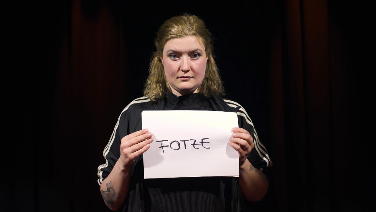 Merle hält ein Blatt Papier vor sich, auf dem "Fotze" geschrieben steht. Merle hält ein Blatt Papier vor sich, auf dem "Fotze" geschrieben steht.