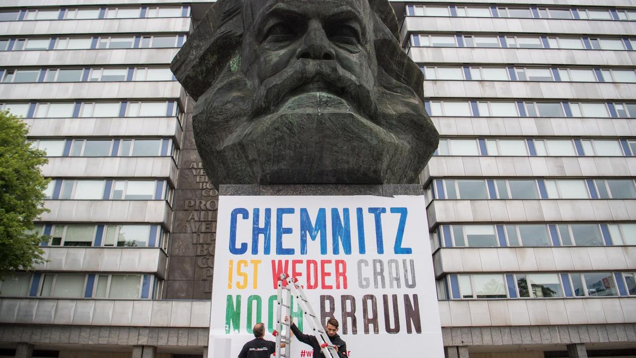 Zwei Männer befestigen am Karl-Marx-Denkmal ein Plakat mit der Aufschrift "Chemnitz ist weder grau noch braun". Zwei Männer befestigen am Karl-Marx-Denkmal ein Plakat mit der Aufschrift "Chemnitz ist weder grau noch braun".