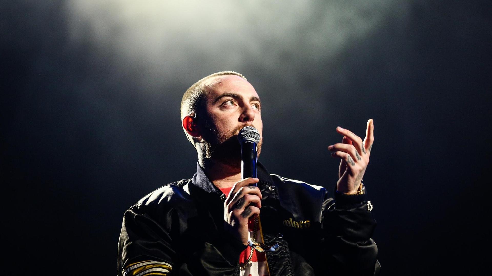 Mac Miller steht mit einem Mikrofon auf der Bühne. Mac Miller steht mit einem Mikrofon auf der Bühne.