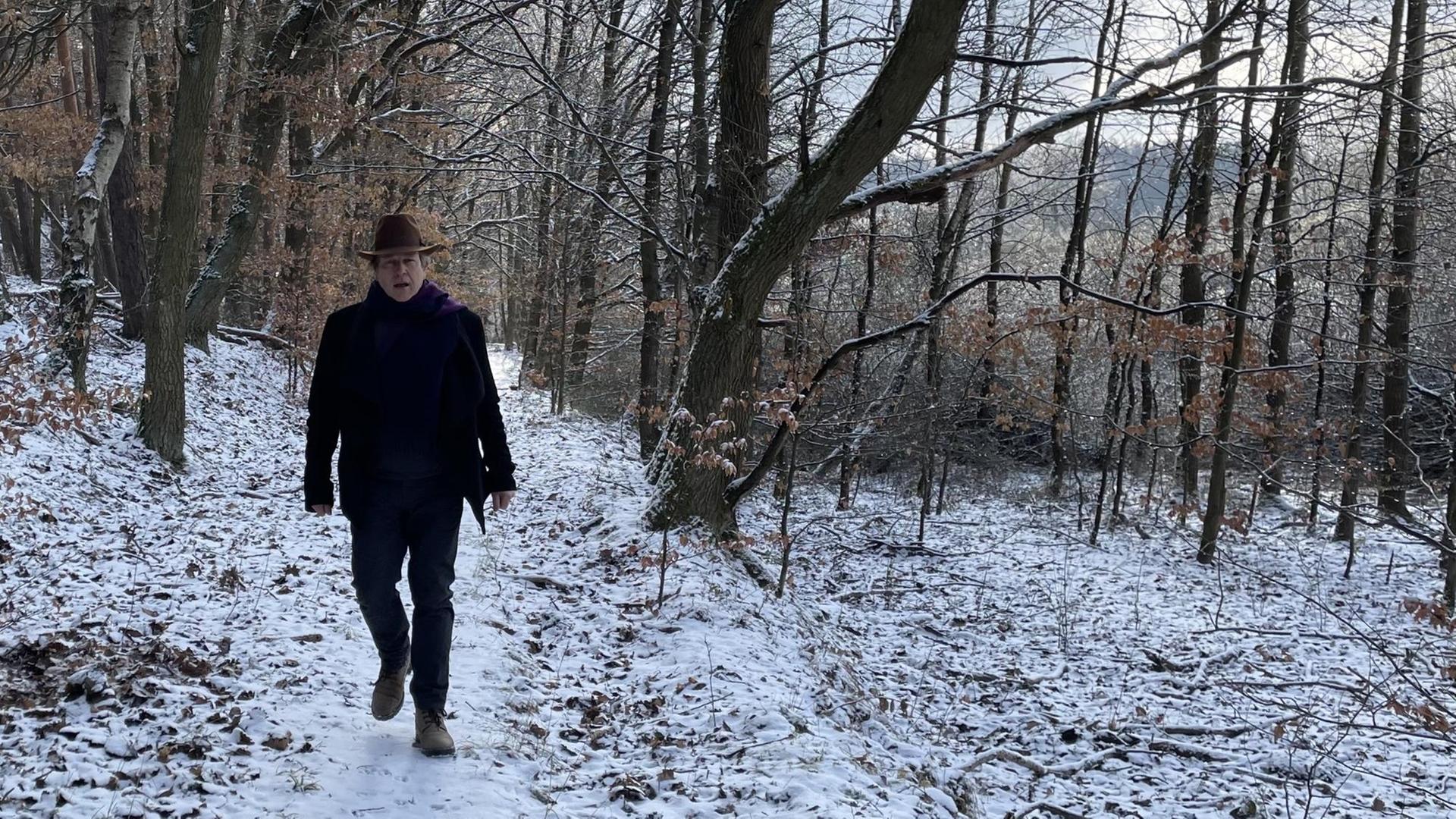 Ein Mann mit Hut läuft durch einen schneebedeckten, lichten Wald. Ein Mann mit Hut läuft durch einen schneebedeckten, lichten Wald.