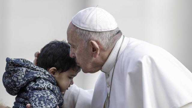 Papst Franziskus küsst in Rom ein Kind auf den Kopf.