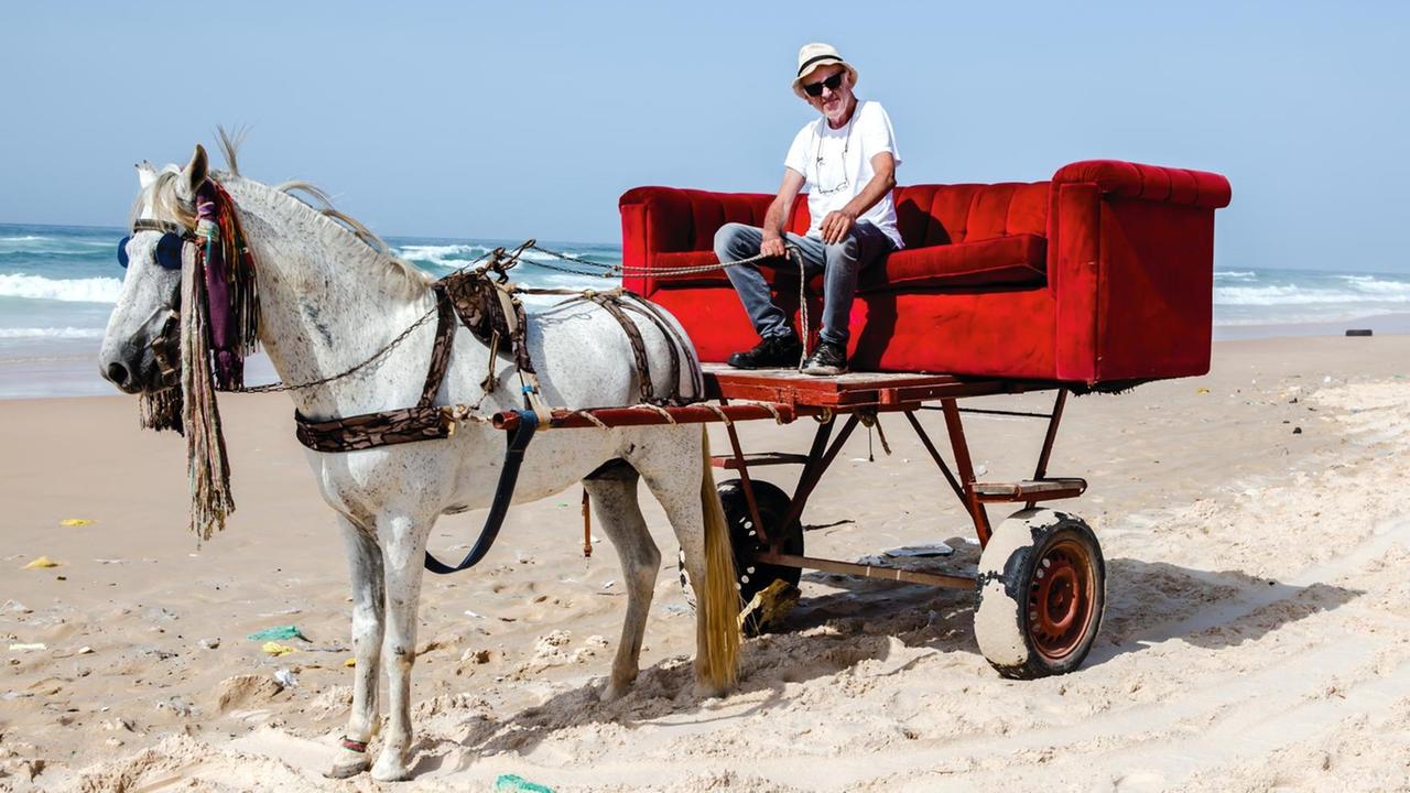 Horst Wackerbart mit seiner Couch auf einer Pferdekutsche an einem Strand im Senegal 2020.