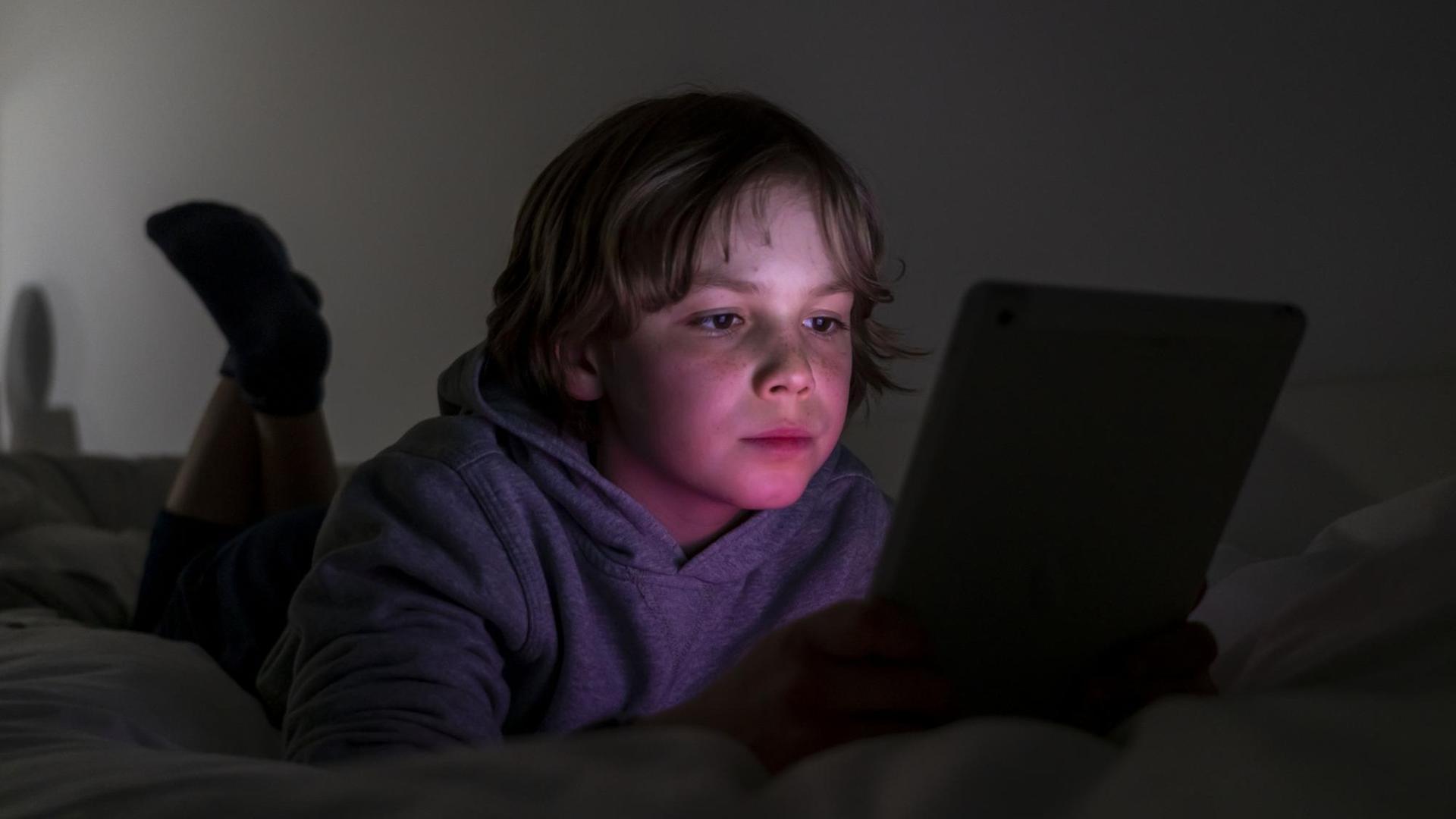 Ein Junge liegt auf einem Bett und spielt Computerspiele an einem Tablet. Ein Junge liegt auf einem Bett und spielt Computerspiele an einem Tablet.
