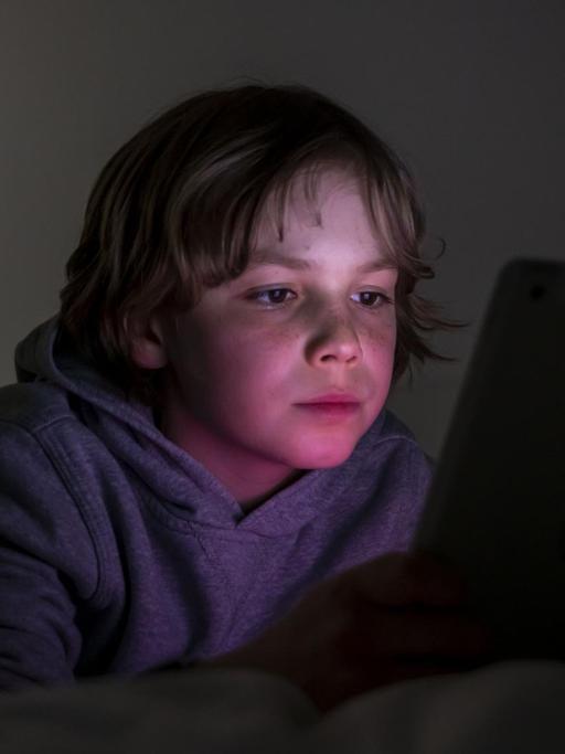 Ein Junge liegt auf einem Bett und spielt Computerspiele an einem Tablet.