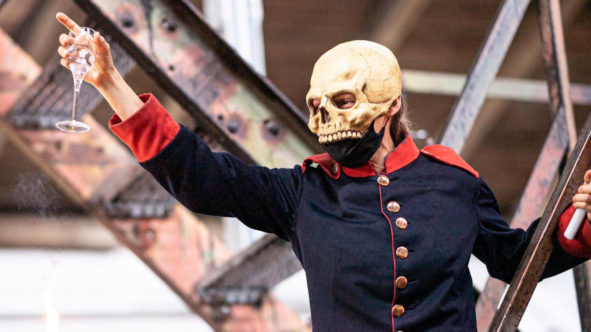 Eine Person in Uniform und mit Totenschädelmaske erhebt feierlich ein Glas Eine Person in Uniform und mit Totenschädelmaske erhebt feierlich ein Glas