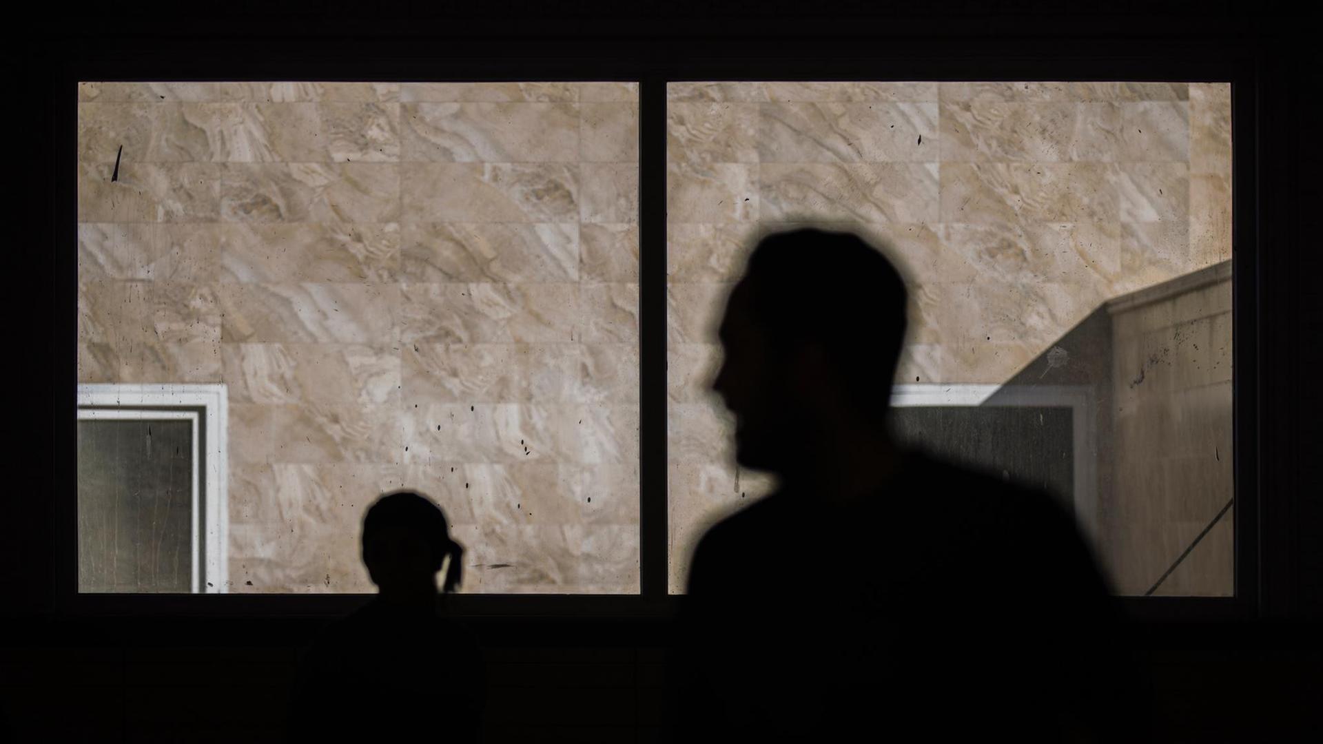 Die schwarzen Silhouetten eines Mannes und einer Frau sind durch ein Fenster zu sehen. Die schwarzen Silhouetten eines Mannes und einer Frau sind durch ein Fenster zu sehen.