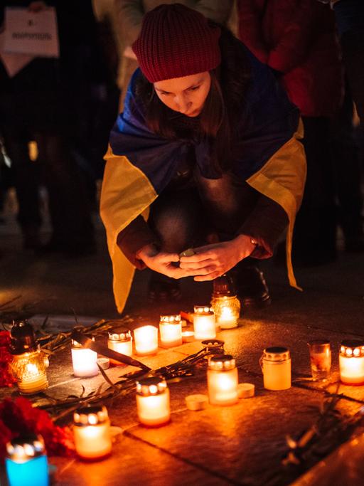 Ein Mädchen trägt eine ukrainischen Flagge über den Schultern und stellt eine Kerze für die Opfer des Raketenangriffs in Mariupol auf der Straße ab.