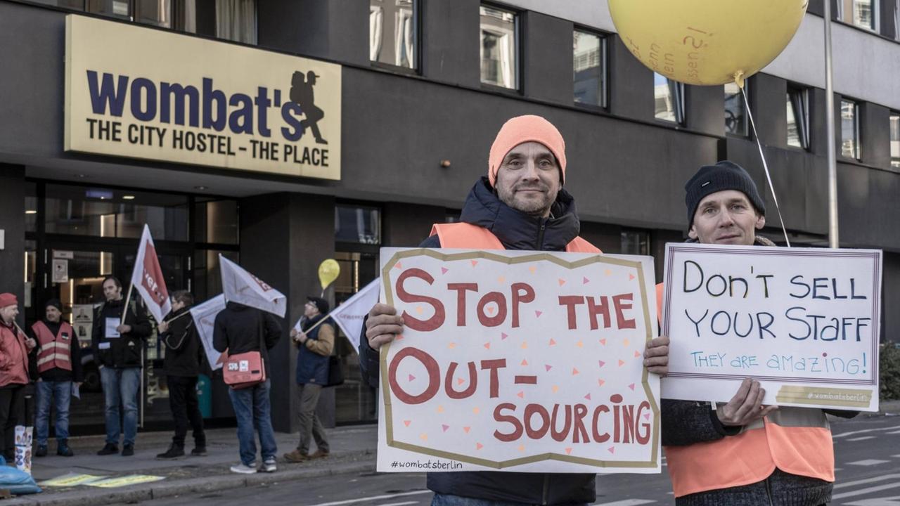 Demonstranten stehen vor einem Hostel und halten Transparente mit Slogans wie "Stop the Outsourcing" hoch. Demonstranten stehen vor einem Hostel und halten Transparente mit Slogans wie "Stop the Outsourcing" hoch.
