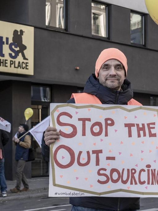 Demonstranten stehen vor einem Hostel und halten Transparente mit Slogans wie "Stop the Outsourcing" hoch.