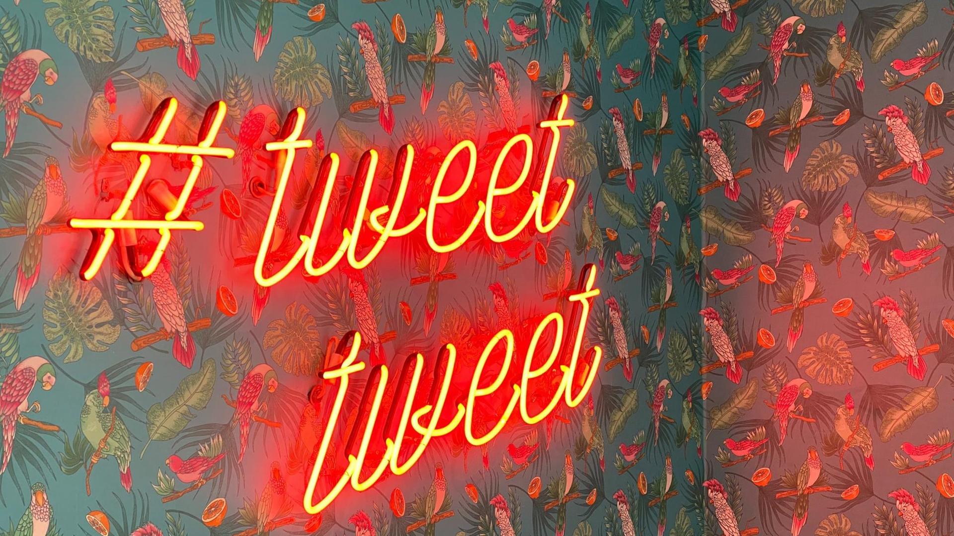 Eine Neonleuchtschrift "#tweet tweet" an einer Tapetenwand.