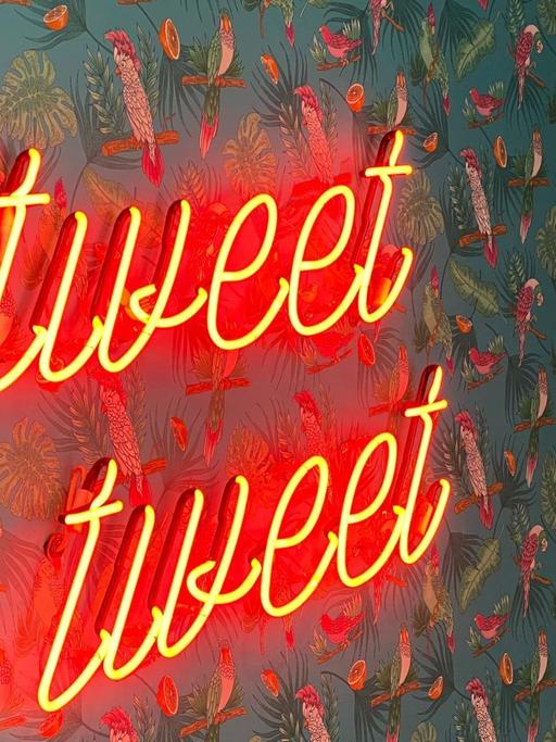 Eine Neonleuchtschrift "#tweet tweet" an einer Tapetenwand.