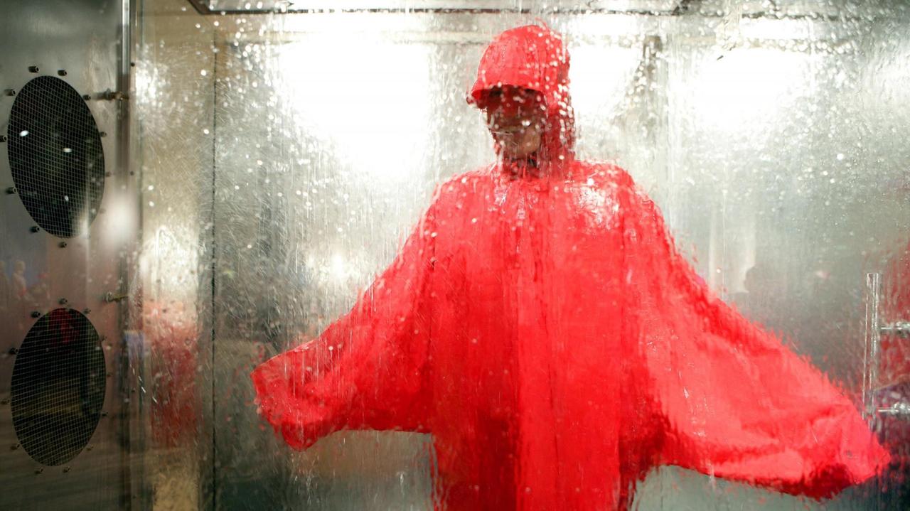 Ein Kunde testet einen Regenponcho in der Regenkammer eines Outdoor-Ladens. Ein Kunde testet einen Regenponcho in der Regenkammer eines Outdoor-Ladens.