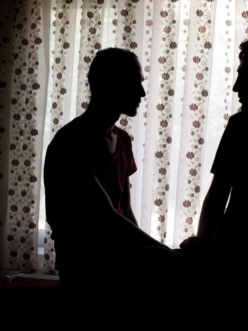 Die Schatten der Partner Danial und Parsa vor einem hellen Fenstervorhang.
