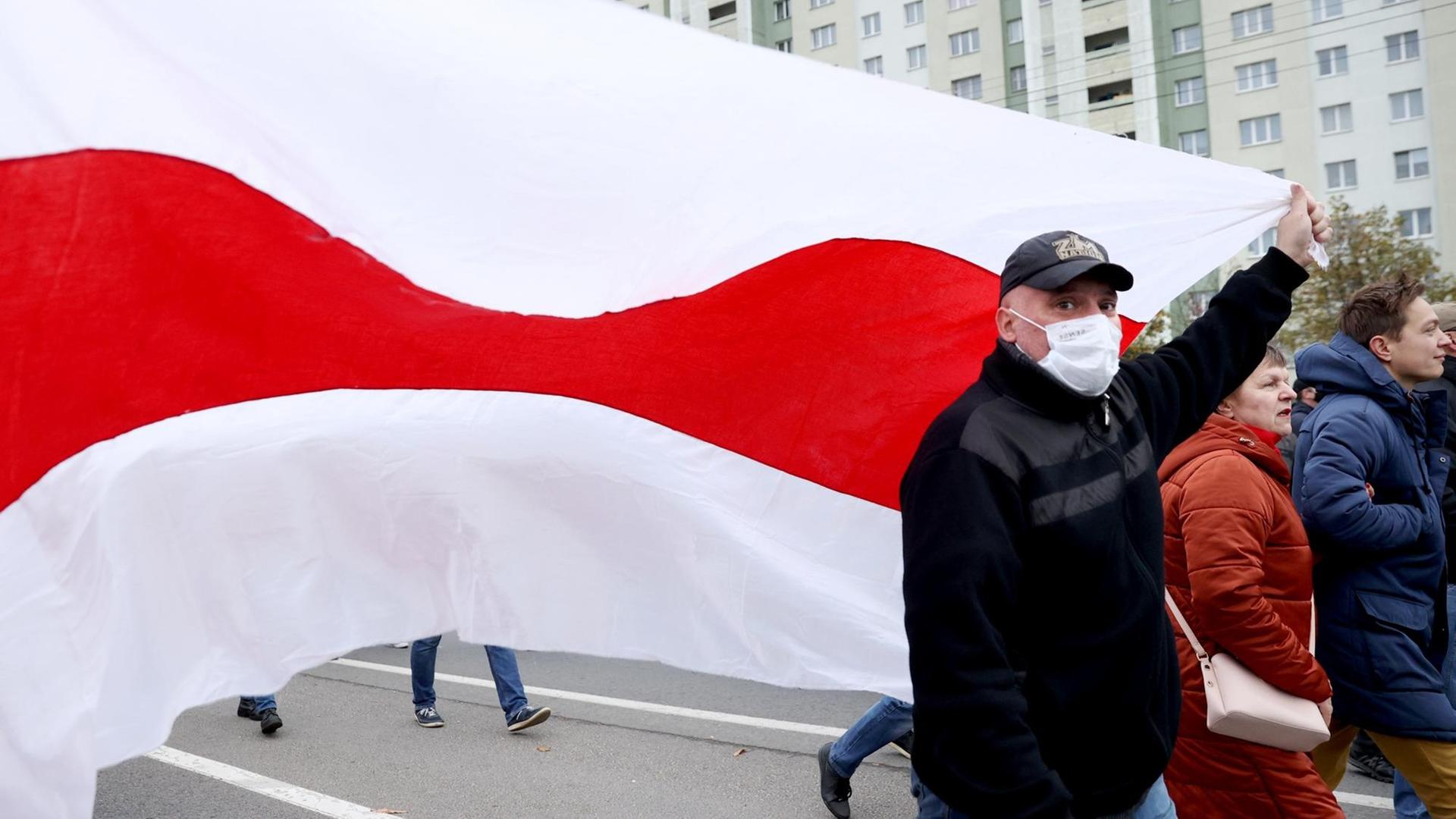 Ein Mann schwenkt die ehemalige weiß-rot-weiße Flagge von Belarus.