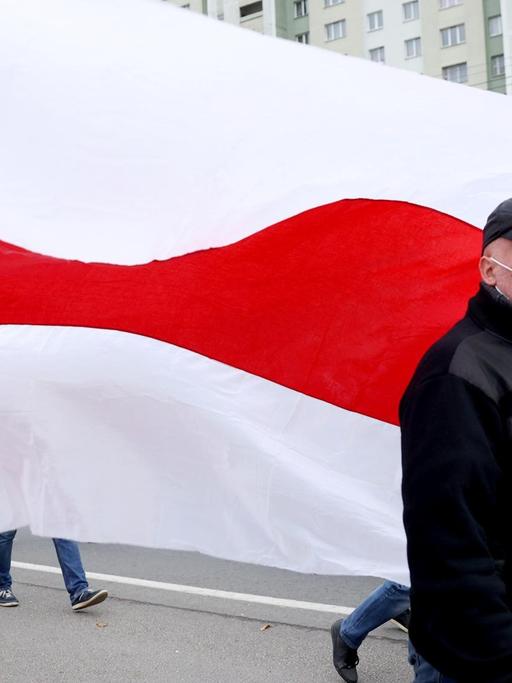 Ein Mann schwenkt die ehemalige weiß-rot-weiße Flagge von Belarus.