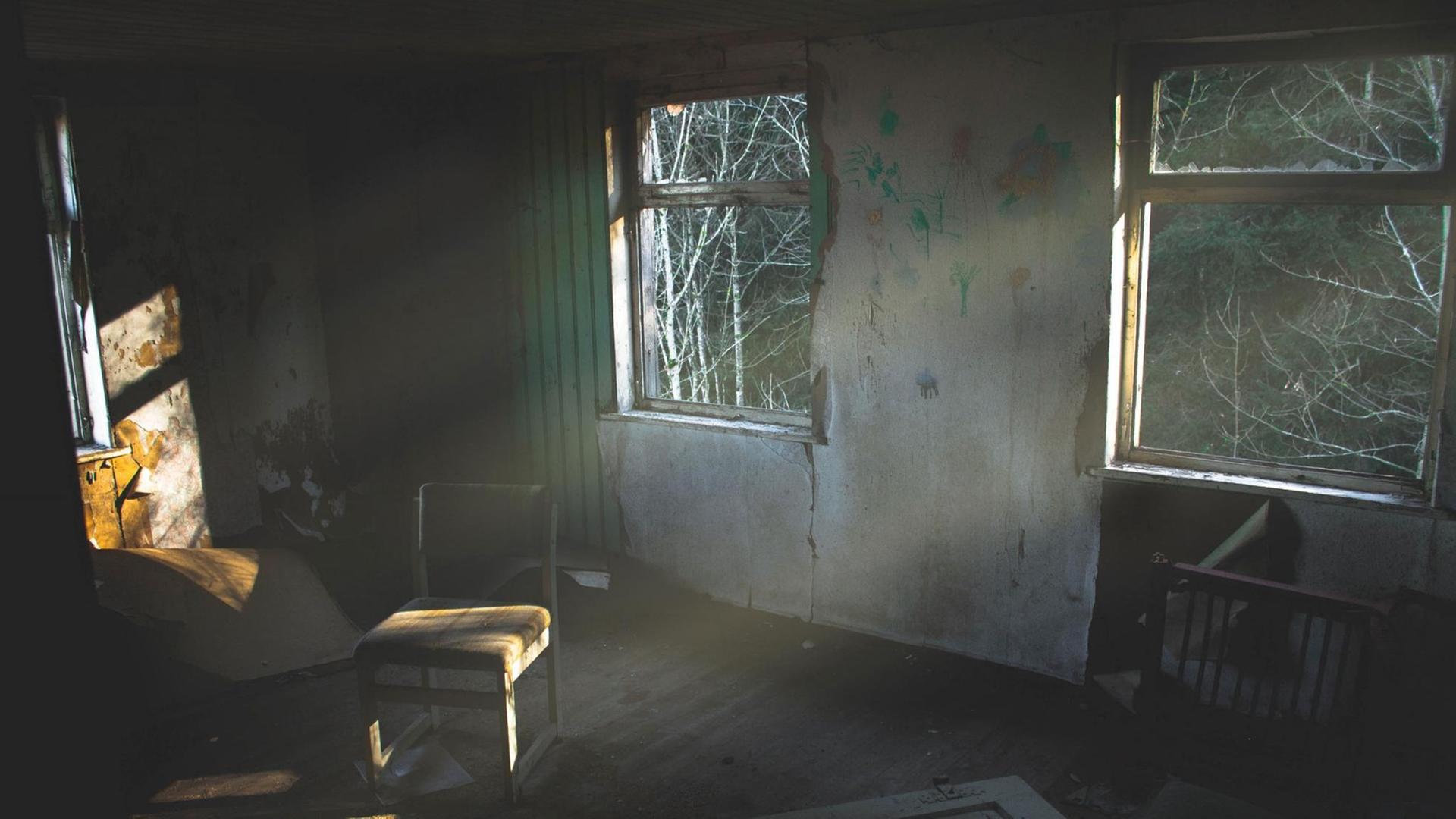 Blick in ein Haus, wo niemand mehr wohnt. Die Fenster sind kaputt, in der Mitte des Raumes steht ein Stuhl.