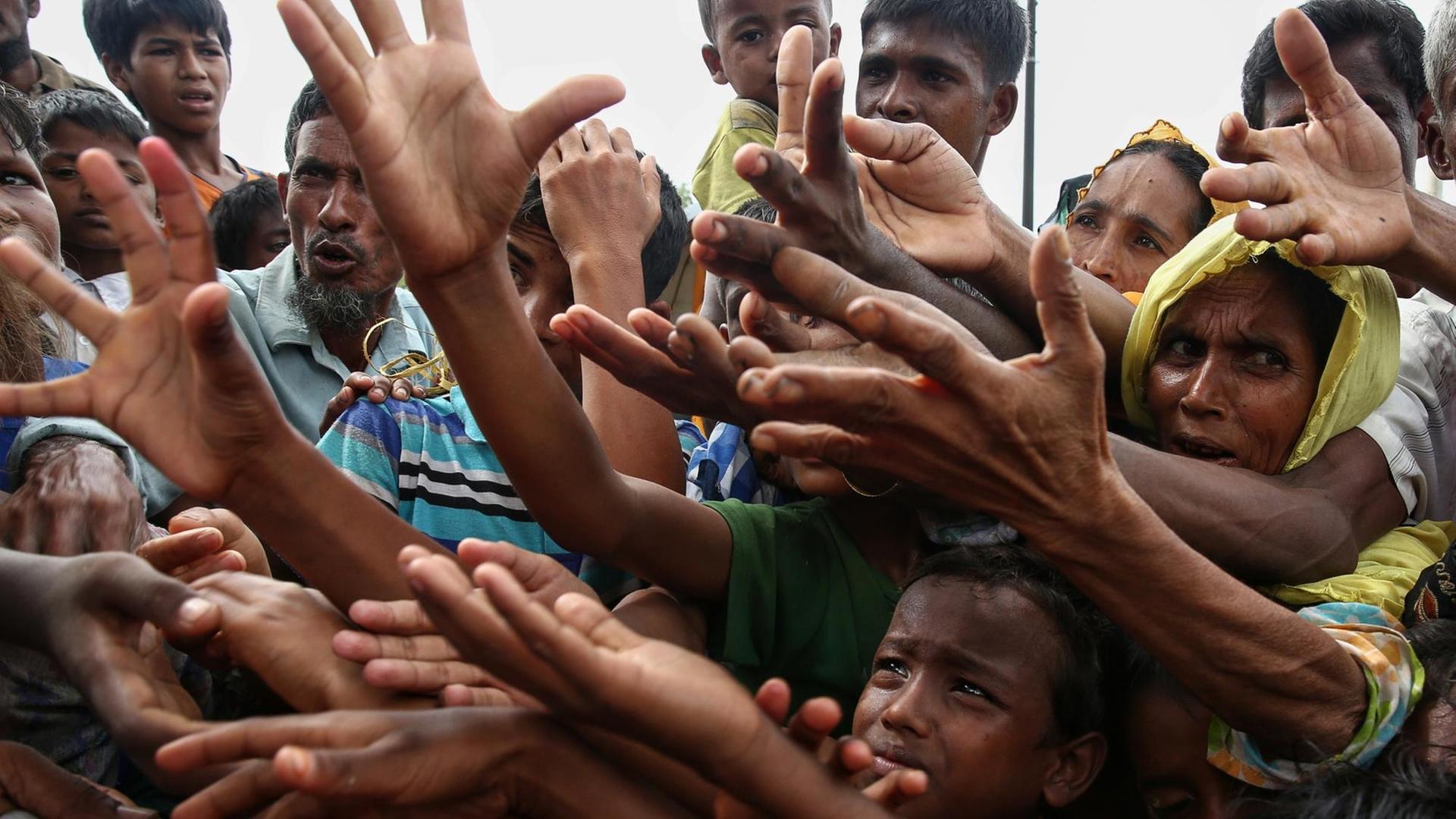 Rohingya-Flüchtlinge strecken in einem Lager verzweifelt die Hände nach Essen aus.