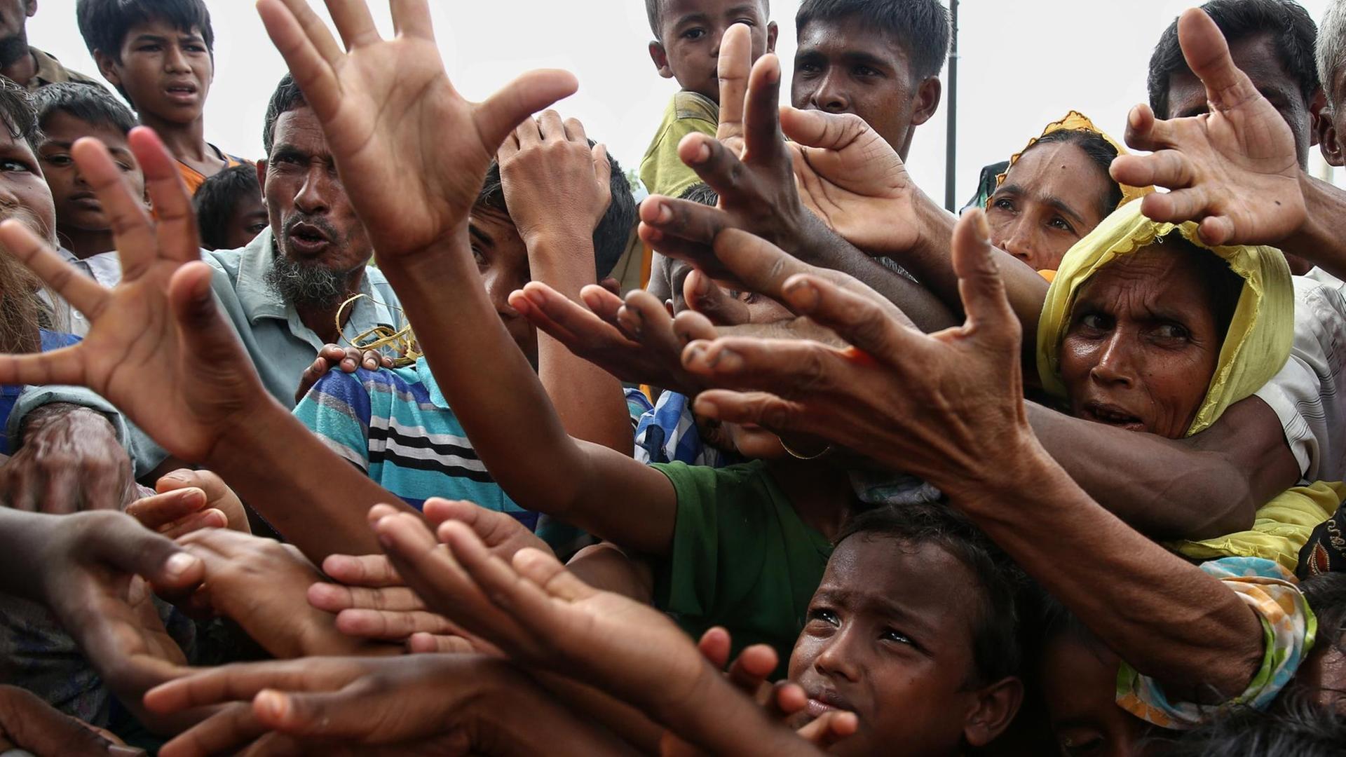 Rohingya-Flüchtlinge strecken in einem Lager verzweifelt die Hände nach Essen aus. Rohingya-Flüchtlinge strecken in einem Lager verzweifelt die Hände nach Essen aus.