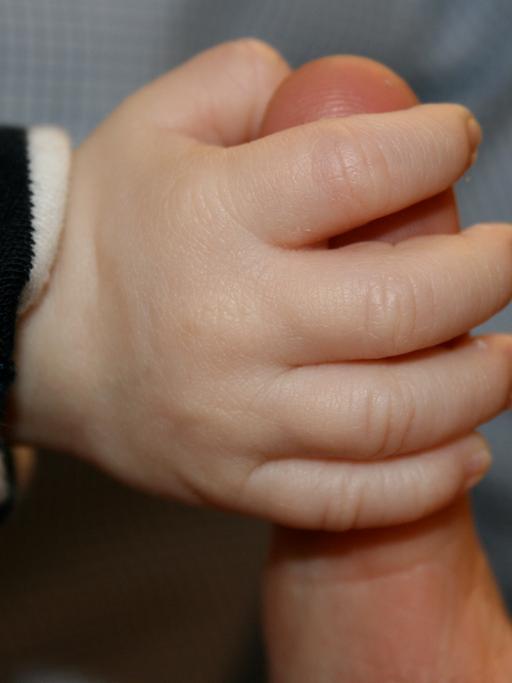 Eine Babyhand umschließt den Finger eines Erwachsenen
