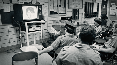 Polizisten sitzen vor einem Röhrenfernseher und schauen Phantombild an.