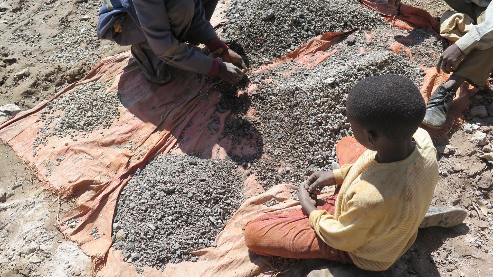 Kinder arbeiten auf dem Boden sitzend in einer Kobaltmine im Kongo. Kinder arbeiten auf dem Boden sitzend in einer Kobaltmine im Kongo.