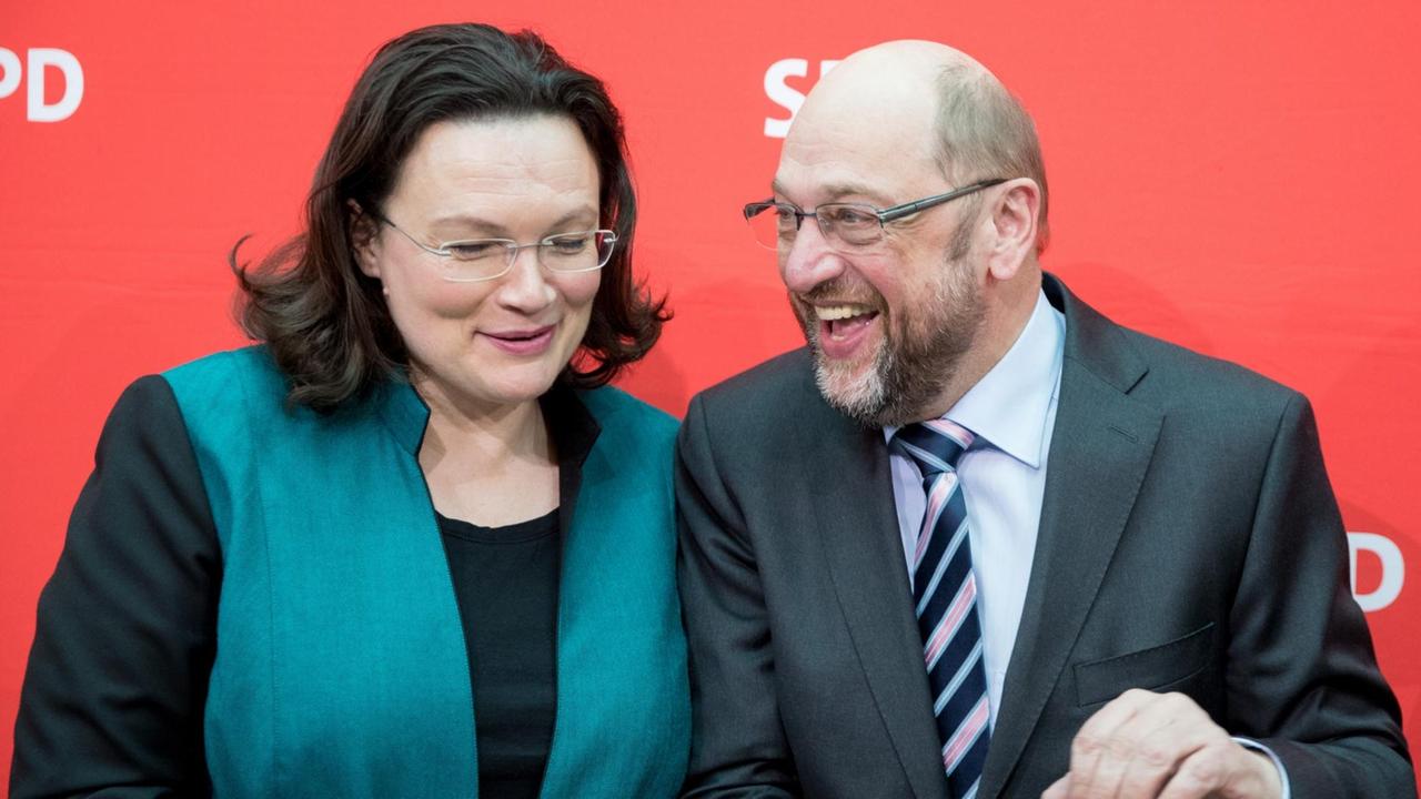 Nahles und Schulz stehen vor einer roten Wand mit dem SPD-Logo und lachen sich zu. Nahles und Schulz stehen vor einer roten Wand mit dem SPD-Logo und lachen sich zu.
