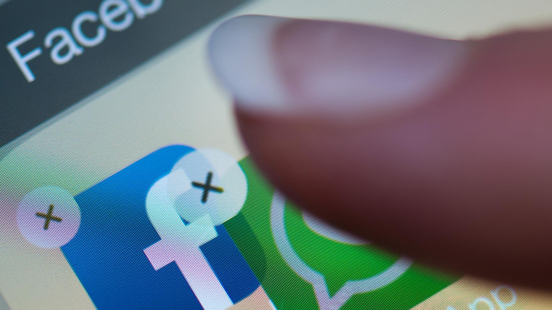 Ein Finger verschiebt auf einem Smartphone-Display die Anwendung "WhatsApp" auf die Facebook-App Ein Finger verschiebt auf einem Smartphone-Display die Anwendung "WhatsApp" auf die Facebook-App