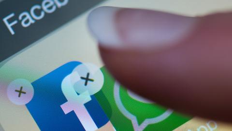 Ein Finger verschiebt auf einem Smartphone-Display die Anwendung "WhatsApp" auf die Facebook-App