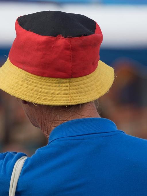 Ein Mann trägt am Rande einer Wahlkampfveranstaltung der AfD Sachsen ein blaues Polo-Shirt und einen Fischerhut in Deutschlandfarben.