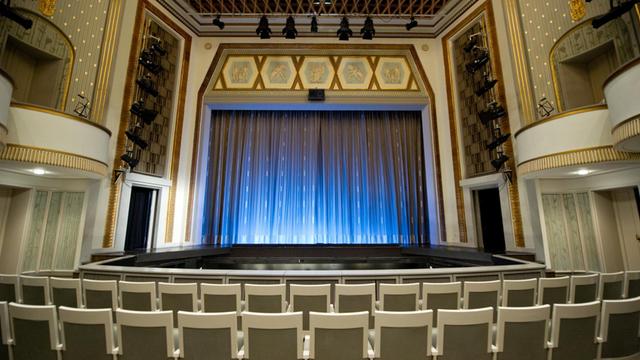 Blick in einen leeren Theatersaal mit geschlossenem Vorhang.