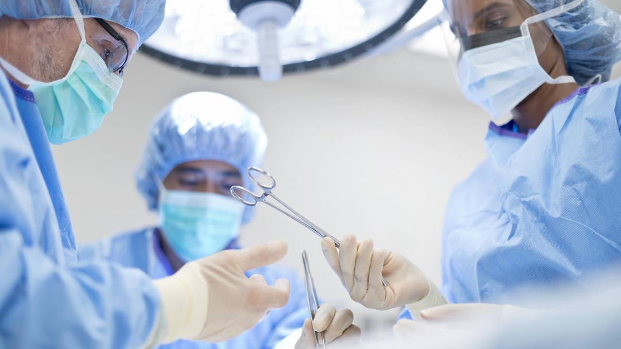 Eine Krankenschwester reicht einem Arzt während einer Operation eine Schere. Eine Krankenschwester reicht einem Arzt während einer Operation eine Schere.