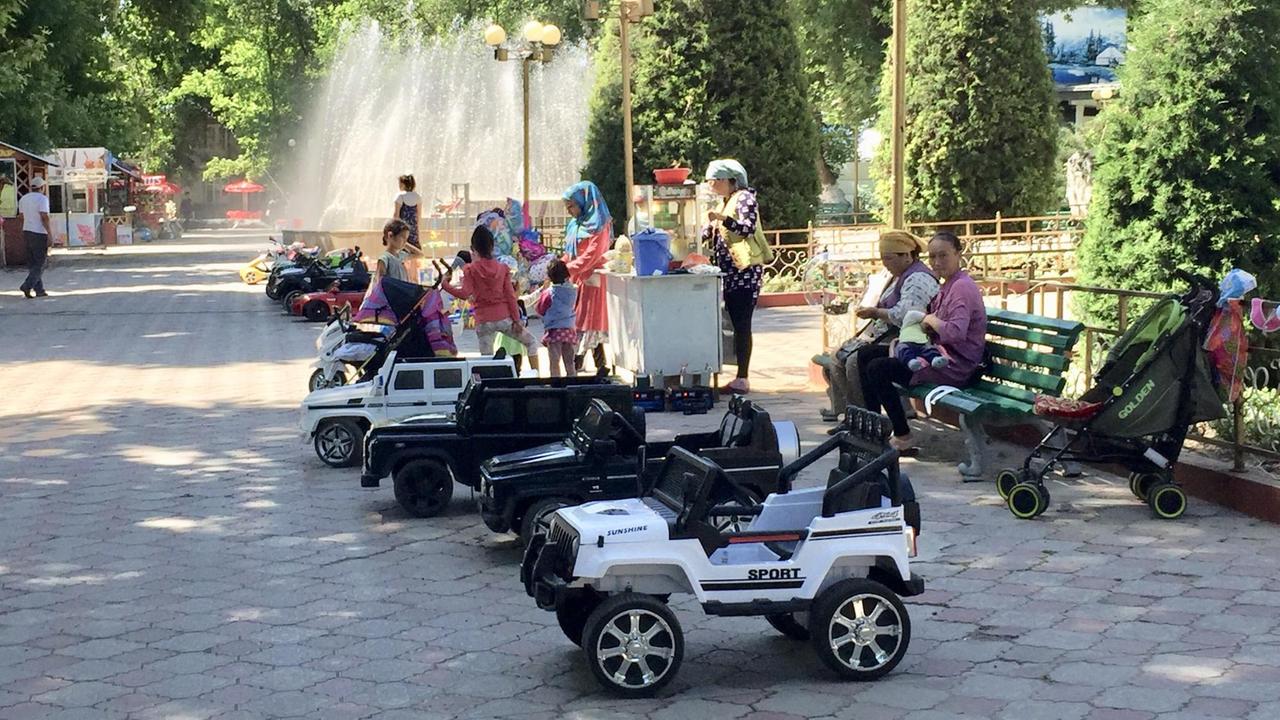 Park, Bänke, mit Mütter udn Kindern, daneben chinesische Spielzeugautos