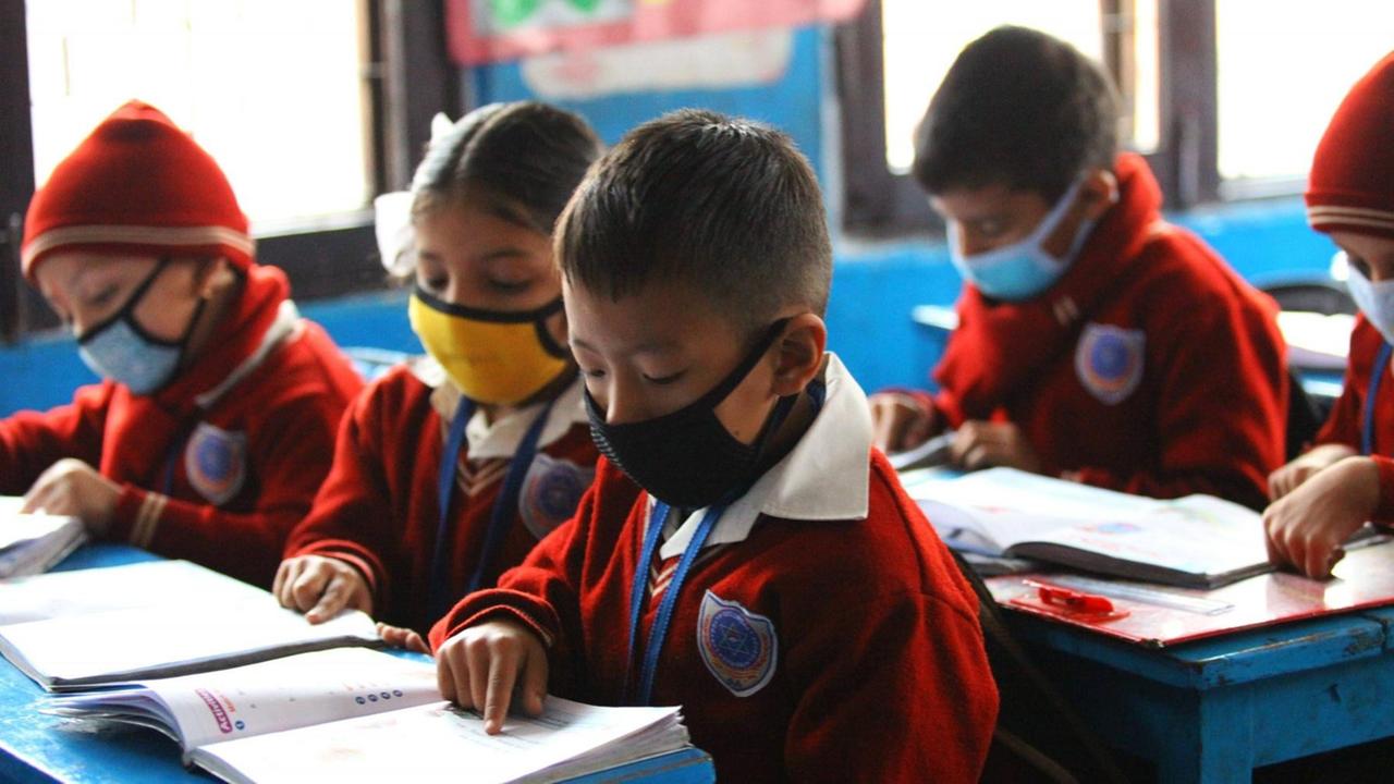 Grundschüler in einer Schule in Nepal sitzen mit Mundschutzen im Klassenzimmer und schreiben in ihre Hefte.