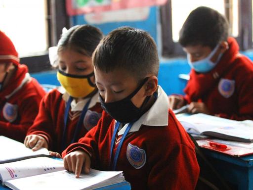 Grundschüler in einer Schule in Nepal sitzen mit Mundschutzen im Klassenzimmer und schreiben in ihre Hefte.